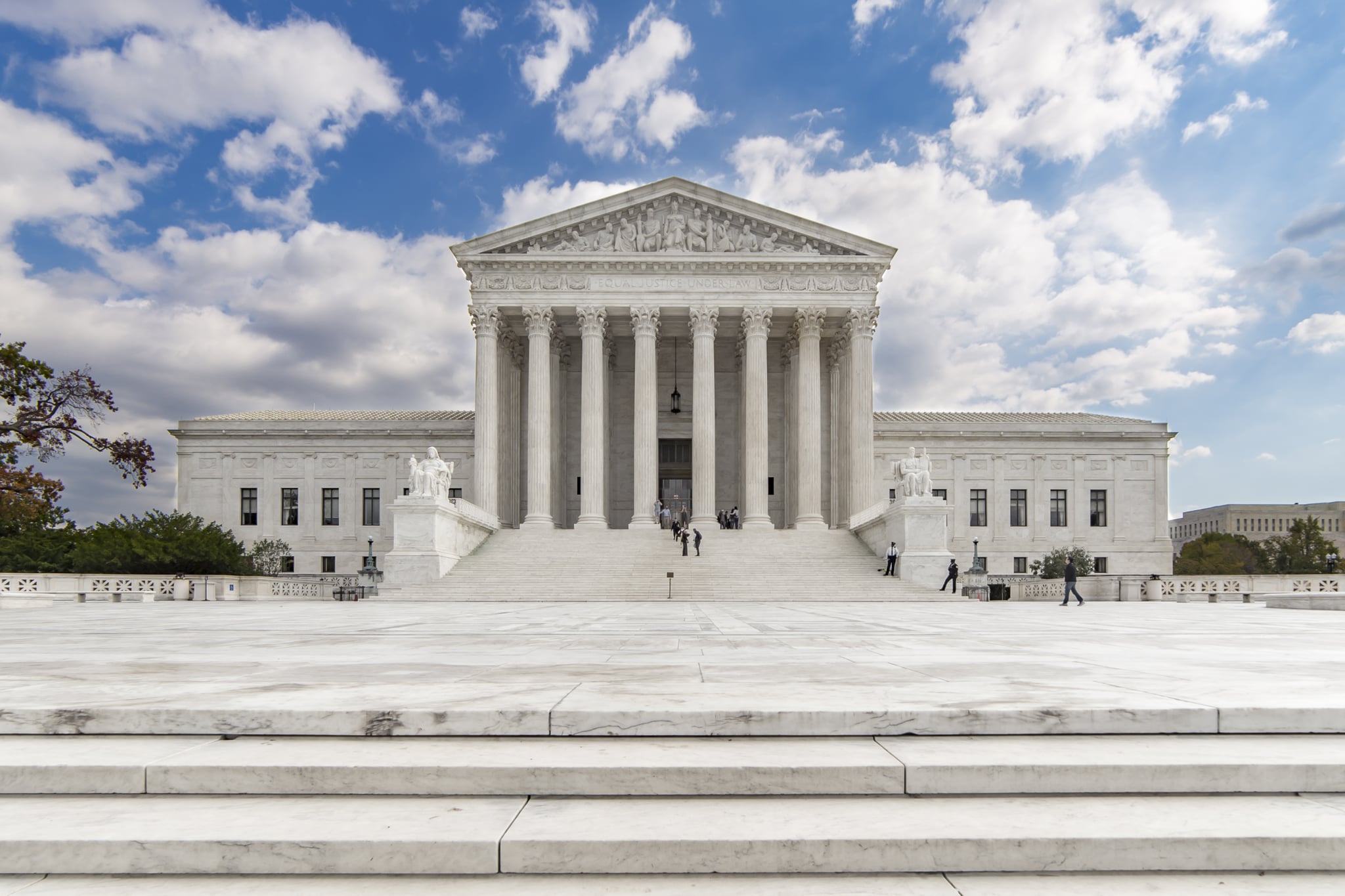Taken at a moment when only a handful of people were in the scene, this straight-on image of the US Supreme Court shows the majesty of the structure. Home to the most powerful lawmakers in the country, this iconic building is centered under a blue sky with some scattered clouds.
