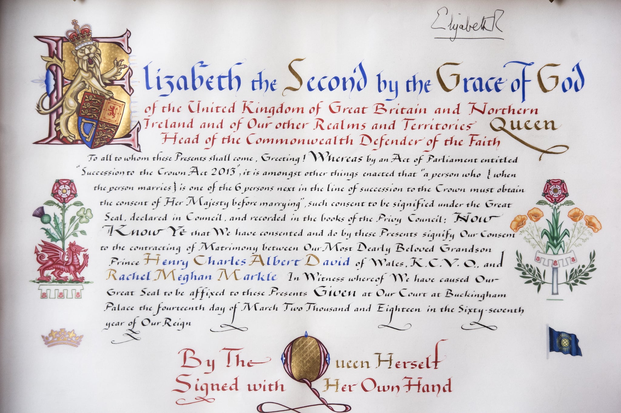 A picture taken at Buckingham Palace in London on April 12, 2018 shows the text and marginalia of the Instrument of Consent, an official State document that records the Queen's formal consent to Prince Harry's forthcoming marriage to Meghan Markle. - The Instrument of Consent is a hand-written document which records Britain's Queen Elizabeth II's consent to the marriage of Prince Harry and Meghan Markle. The document is hand-written and illuminated on vellum and sealed with the Great Seal of the Realm. The Queen's signature, 