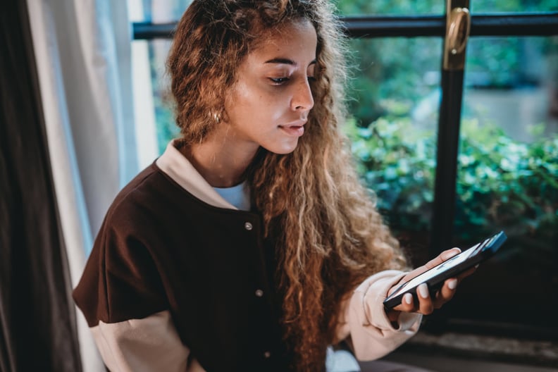 Young adult woman is checking her bank account. She's holding a smart phone with a bank mobile app.