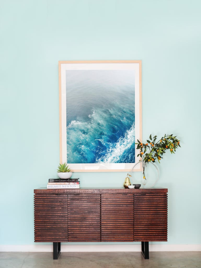 For the makeover, Whitney explains, "We wanted to make sure the white walls were filled with tons of artwork and that the furniture was cozy and inviting." Orlando responded by painting the walls a cheerful Robin's-egg blue and adding beachy accents like this oversized ocean print and warm wooden console.