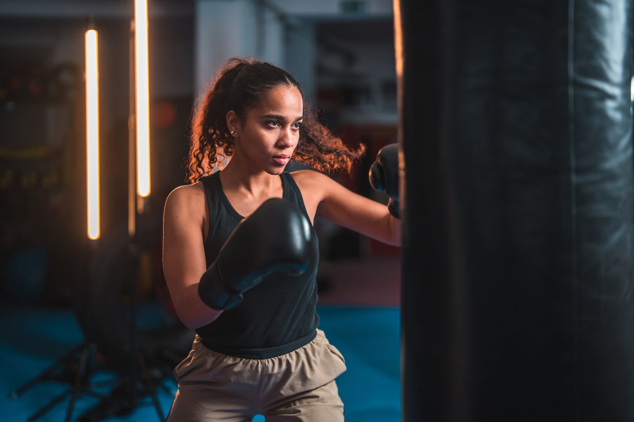 Determined, tough young female boxer shadowboxing in gym