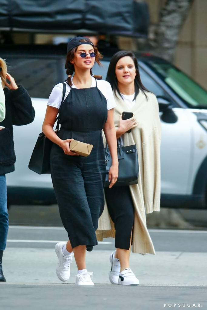 It looks like Selena Gomez certainly knows her '90s style icons. After channeling her inner Rachel Green, Selena has moved on to the real deal and seems to be taking style notes from Jennifer Aniston herself — they are friends IRL, after all. In a recent Instagram story, Selena's friend Connar Franklin shared a side-by-side comparison of the singer's chic weekend outfit and Jennifer's ensemble from the 1997 film Picture Perfect — and it totally looks like Selena raided Jennifer's closet. On her way to a church service over the weekend, Selena wore a black jumpsuit layered over a white t-shirt, putting a slight twist on Jennifer's original spaghetti strap dress outfit. Selena finished off the look with loose pig tails, a black baseball cap (worn backwards, of course), and a pair of the teeny tiny sunglasses that never seem to go out of style. Selena accessorized with an over-sized purse that pulled the look together and — short of wearing a Walkman — made the singer look just like her Picture Perfect inspiration. Needless to say, we're in love with this outfit and we'd love to see Selena recreate Jennifer Aniston's entire '90s wardrobe. See how spot-on her outfit was compared to the original ahead.