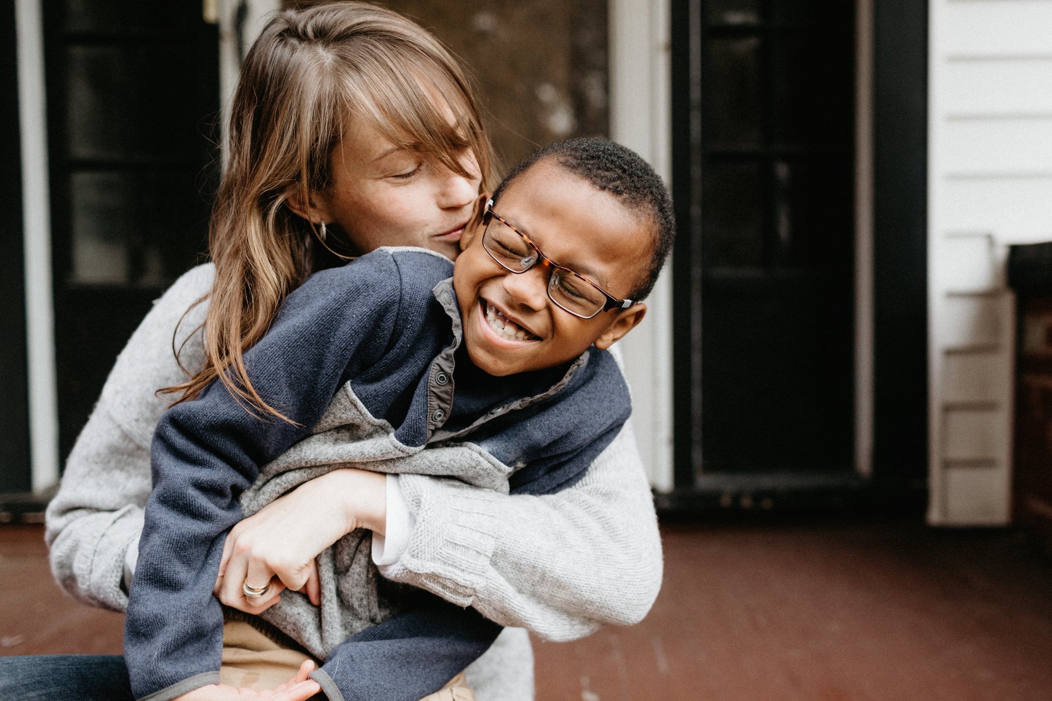 A mother and her adopted son smiling, laughing and cuddling on the front porch in buffalo new york in november