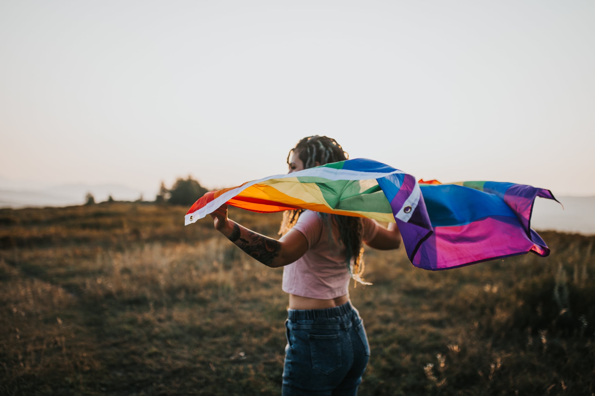 woman holding LGBTQ+ pride flag in front of sunset outdoor
