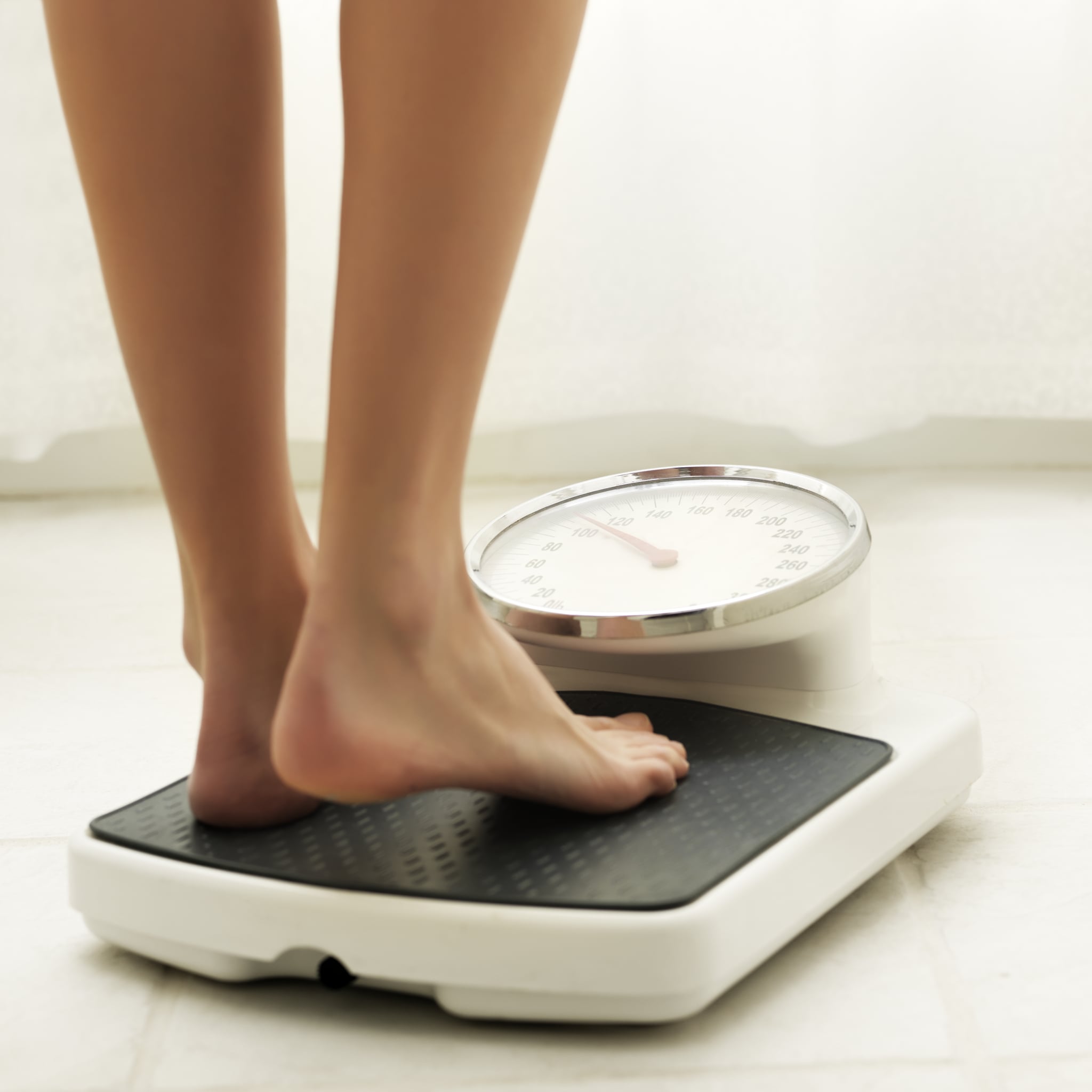 Young fit woman stepping on a bathroom scale. Square shot.