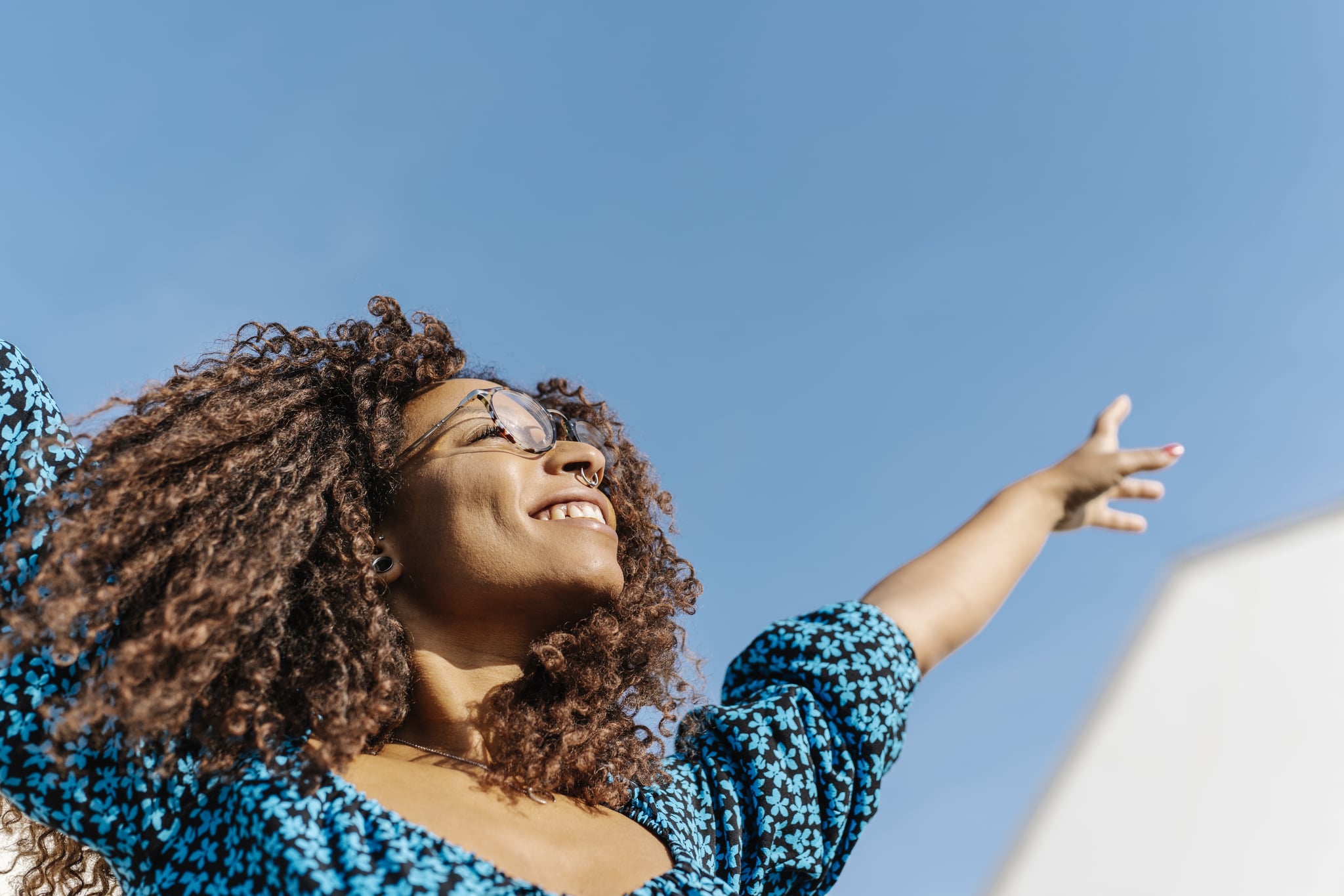 Young woman with African roots raising her arms with a blue sky in the background. Happiness concept
