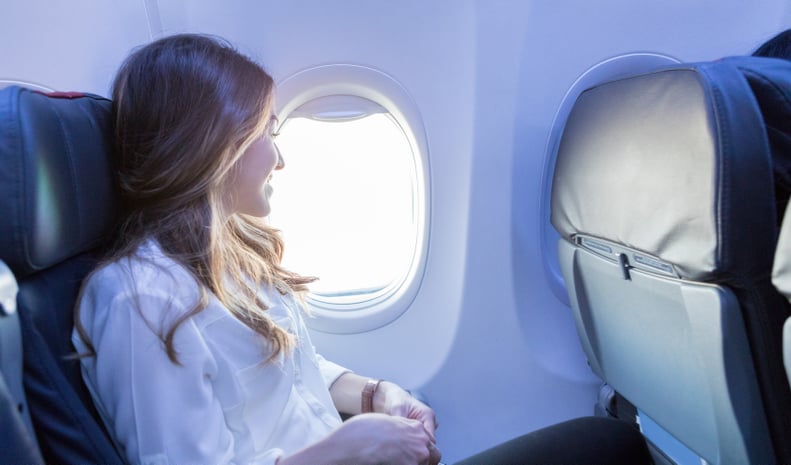 In this side view, a smiling young woman enjoys looking out the window of her aircraft as she awaits arrival to her destination.