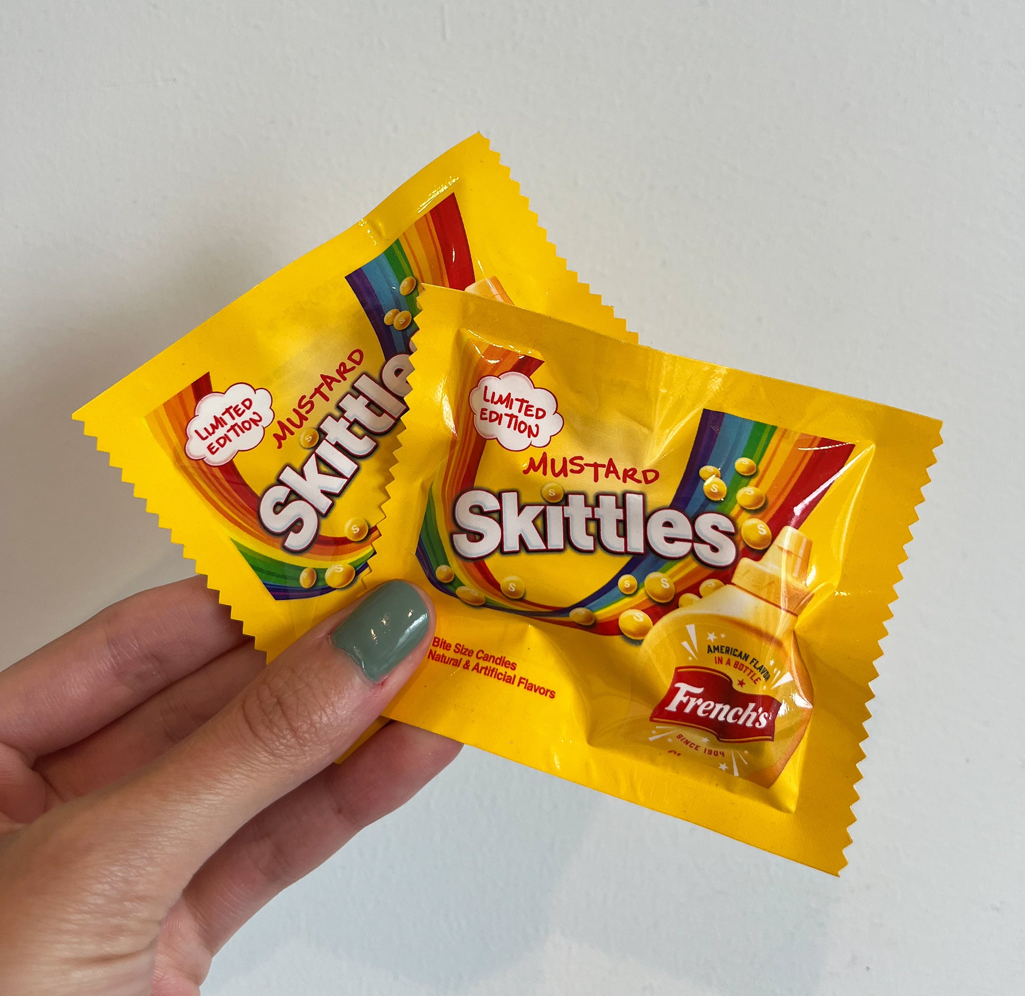 Two packages of French's mustard-flavoured Skittles candies.