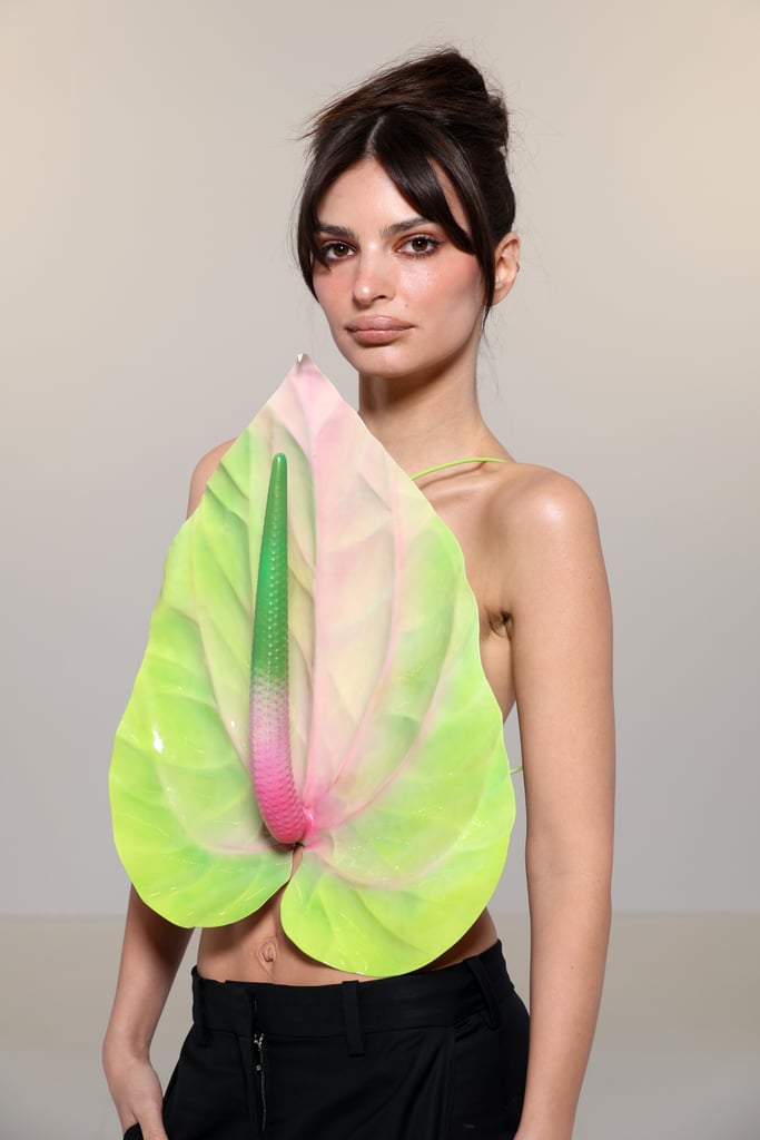 Emily Ratajowski is turning over a new leaf. On March. 3, the model arrived at Paris Fashion Week for the Loewe fall 2023 runway show wearing a faux anthurium flower top. The eccentric design featured skinny chartreuse straps hidden underneath her plant-inspired look. From the center of the backless shirt, a hyper-realistic stigma emerged, fading from dark pink to bright green. She paired the standout piece with low-waisted trousers and sandals, sweeping her hair into a high bun to show off every detail of the flower. 
While her leaf top definitely stood out from her front row seat at the show, having fun with fashion is nothing new for Ratajkowski. Previously, she's stepped out in everything from polarizing thigh-high knee socks to an entirely fishnet dress. In fact, some of her fashion has been so controversial, she still remembers the drama years later, previously referring to a particular plunging dress she wore to the 2016 Harper's Bazaar Icons party as "the most controversial dress I've ever worn."
"I was basically called out for wanting attention, which I think is interesting because you go to red carpets for attention, basically," she said in a video with Harper's Bazaar from October 2022. Now, Ratajkowski continues to keep her fans on their toes with naked dresses and a singular leaf as a top. 
Anthuriums, also called flamingo flowers, are known for their bright coloring and unique shape. But considering their reputation as tropical plants with a fondness for humidity and warmth, Ratajkowski's look was a surprisingly vibrant choice for a cloudy March day in Paris. Could this be the model's way of ushering in brighter days? Check out her full outfit below.

    Related:

            
            
                                    
                            

            Noah Cyrus Goes Braless in a Sheer Hooded Dress at Milan Fashion Week