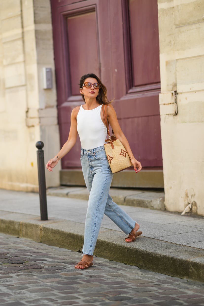 PARIS, FRANCE - JULY 20: Alexandra Pereira wears brown sunglasses from Tod's, a white ribbed tank top, a beige large wicker bag from Vuitton with printed monograms, pale blue denim ripped jeans pants, brown leather Hermes Oasis sandals / shoes, on July 20
