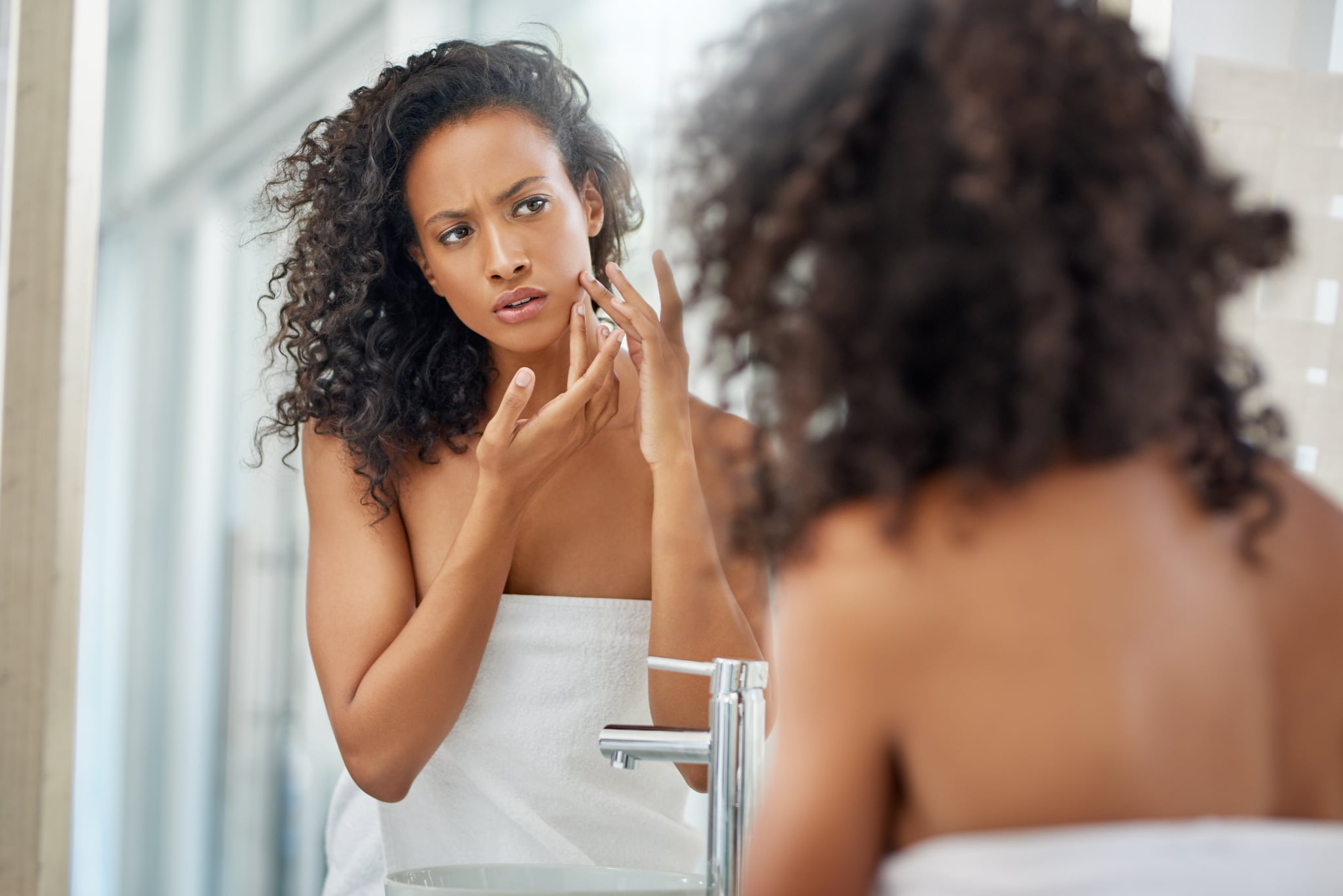 .Shot of an attractive young woman inspecting her face in the bathroom mirror