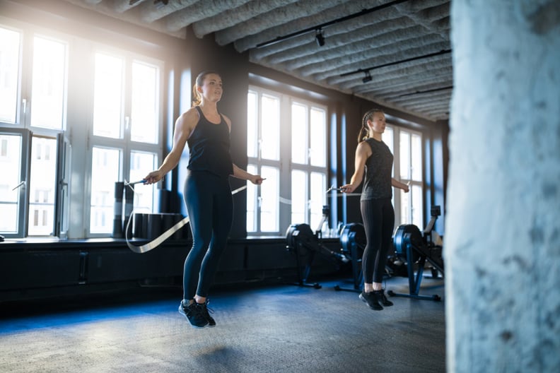 年轻女性做锻炼在健身房跳绳索。确定女运动员在健身俱乐部锻炼。他们在体育服装。