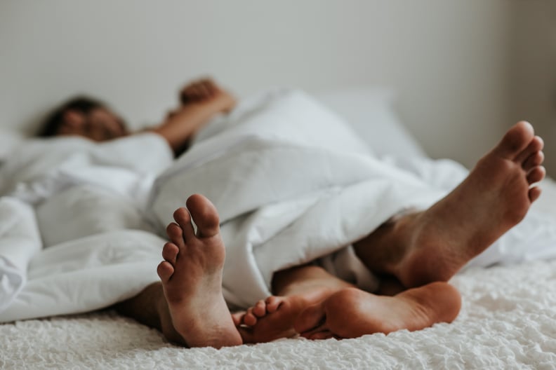 A couple cuddles and kisses in bed. Their feet are in the foreground of the photo.