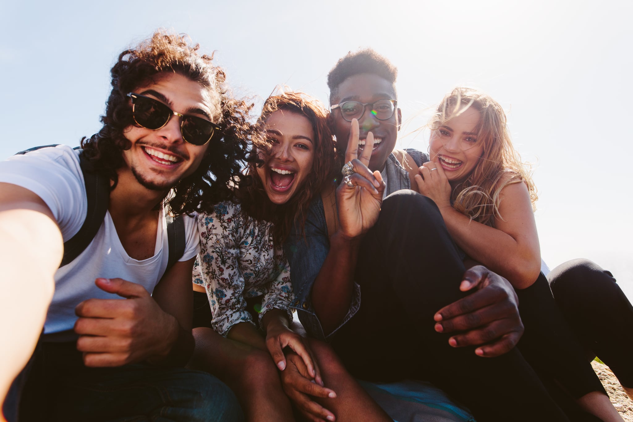 Excited young friends taking selfie outdoors. Diverse group of men and women sitting together and taking self portrait on their holiday.