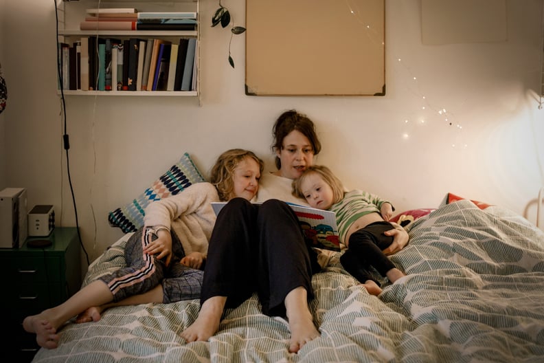 A solo mom reads a book to her two young kids in their pajamas at bedtime.
