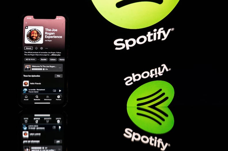 This picture taken in Toulouse, southwestern France, on January 31, 2022 shows a smartphone displaying the Joe Rogan podcast and a screen displaying the Spotify's logo. - Caught in a disinformation maelstrom, Spotify announces it will guide listeners of C