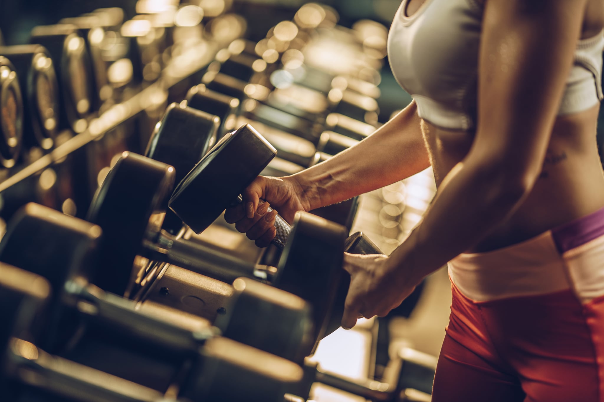 Unrecognisable muscular build athlete taking dumbbell from the rack in a health club.