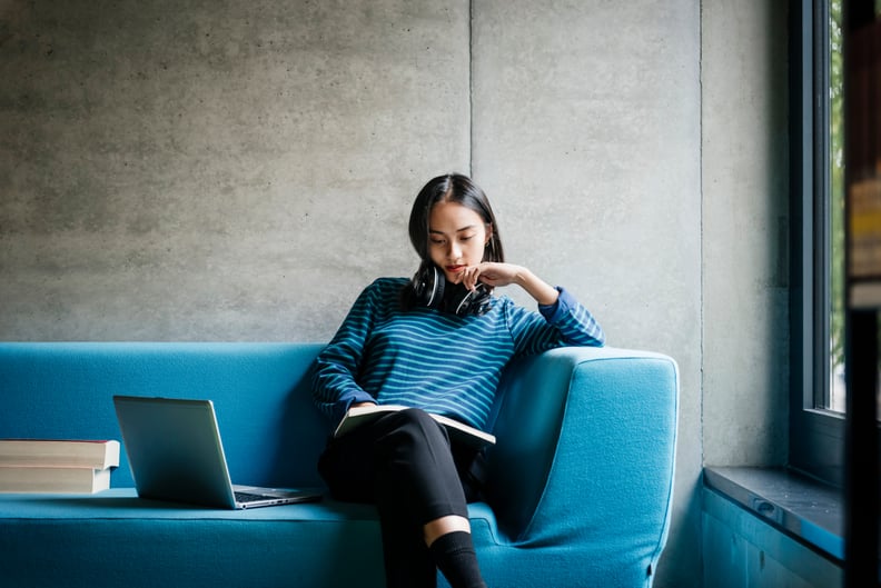 A young woman sitting on a couch looking at a laptop in a quiet library space.