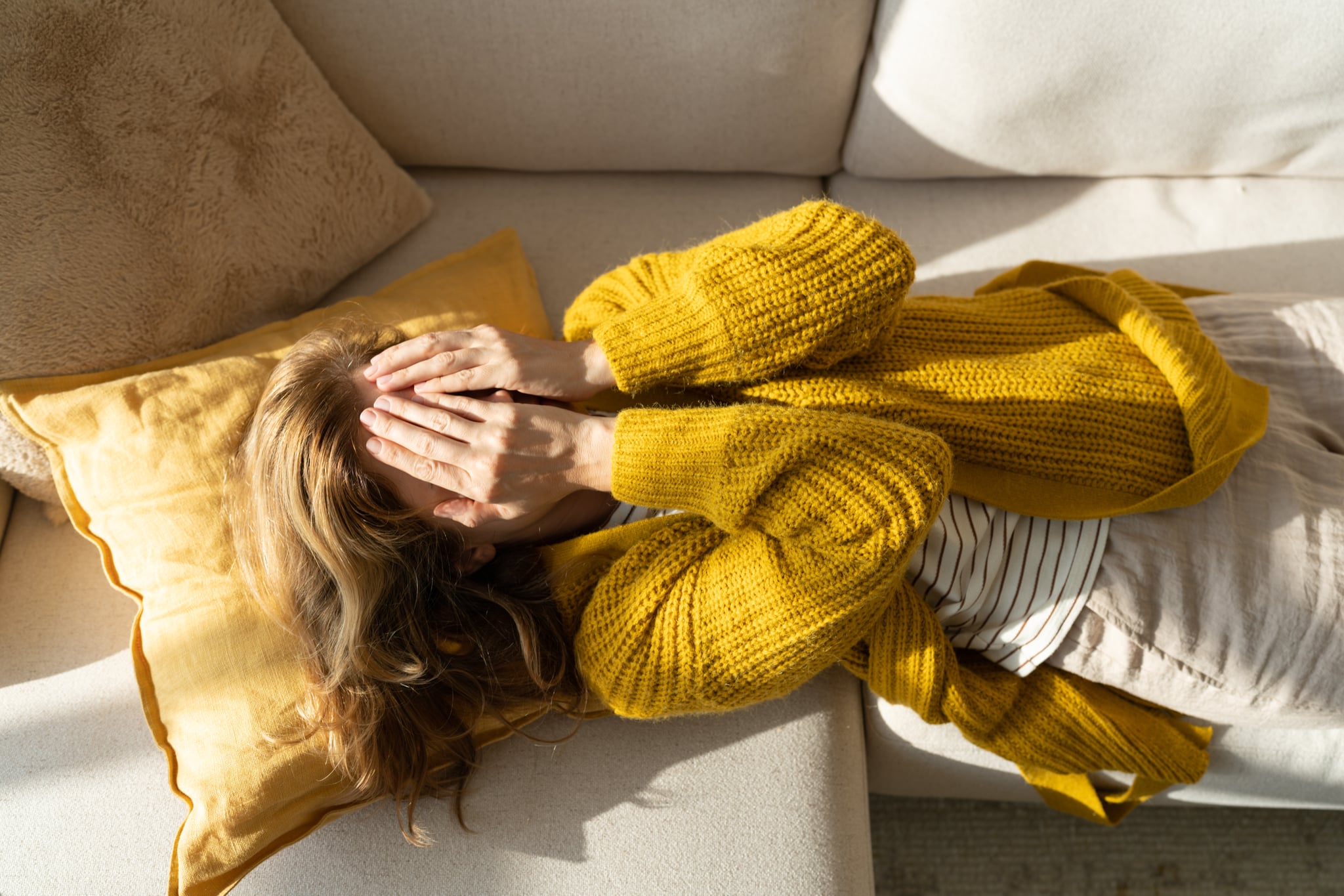 Tired woman lying on sofa while holding hands on her face, overstimulation.
