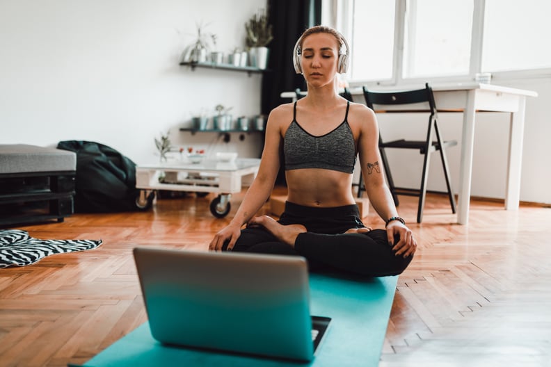 Beautiful young woman using laptop and headphones while meditating and practicing yoga at home
