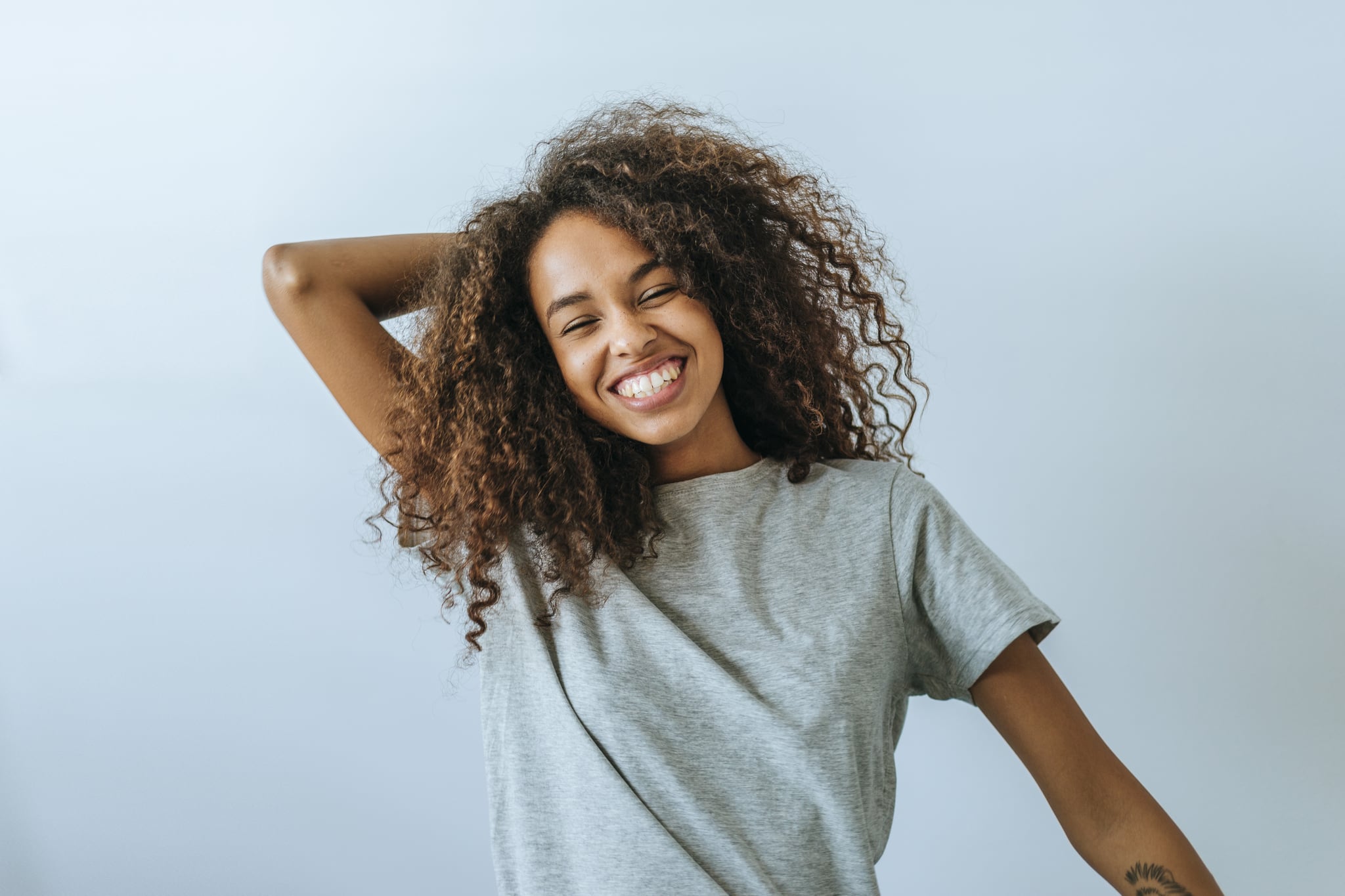 Portrait of woman with afro hair smiling with white wall background.