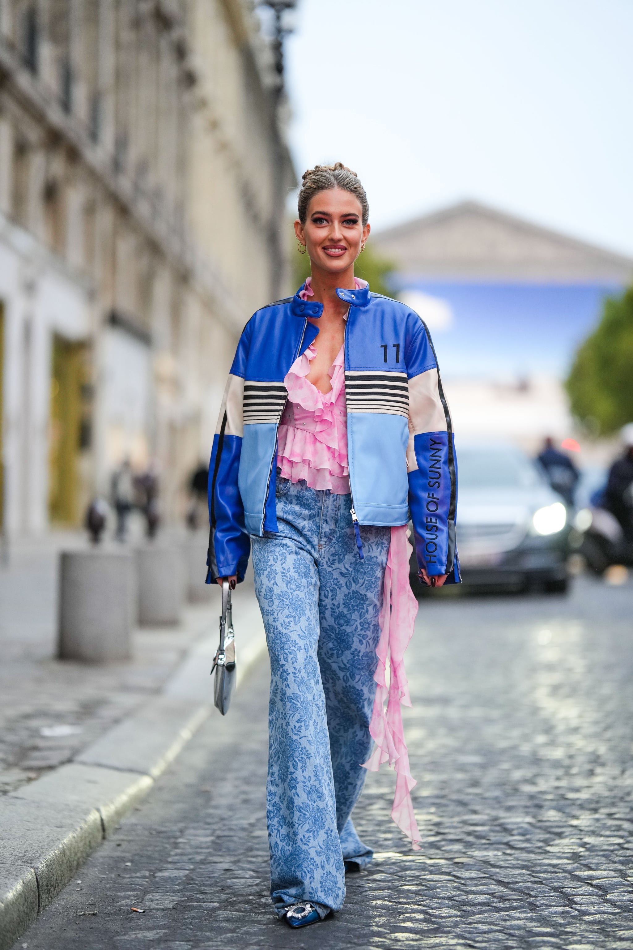 PARÍS, FRANCIA - 30 DE SEPTIEMBRE: Emili Sindlev usa aretes dorados, una corbata rosa pálido y blanca y un patrón de tinte con volantes / blusa con cuello en V de pedrería bordada con un cinturón colgante largo, una cremallera de cuero brillante azul marino / blanco / negro / azul pálido Chaqueta, corbata azul y teñido con estampado de flores, grandes pantalones de mezclilla, un bolso Cleo de cuero plateado brillante de Prada, plástico azul con pedrería bordada, puntera con hebilla/zapatos de tacón puntiagudos, en las afueras de Alessandra Rich, durante la Semana de la Moda de París - Moda femenina Primavera/Verano 2023, el 30 de septiembre de 2022 en París, Francia.  (Foto de Edward Berthelot/)