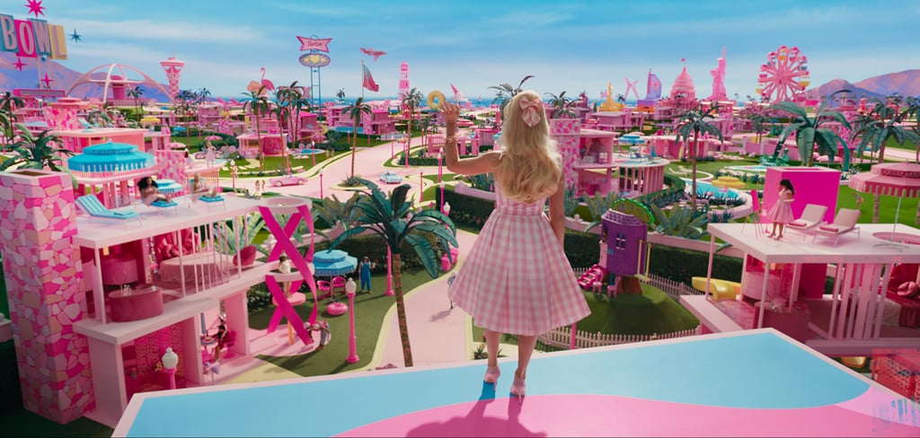 罗比身穿粉色格子a字裙和蝴蝶结套装，搭配粉色高跟鞋，俯视“芭比世界”。