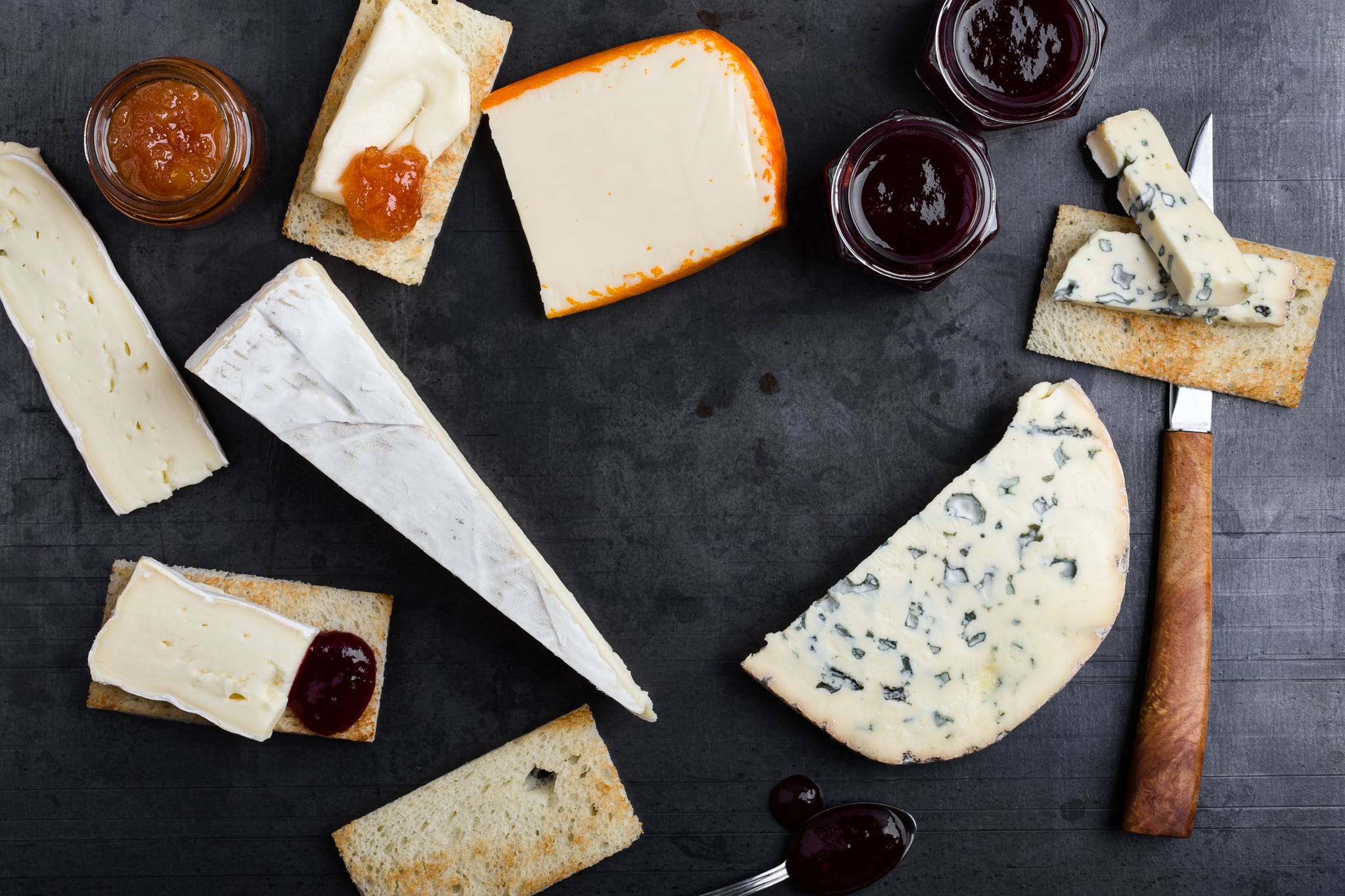 Various types of French cheese with jam over grey background viewed from above. Creamy Saint Paulin cheese, brie, Fourme d'Ambert blue cheese