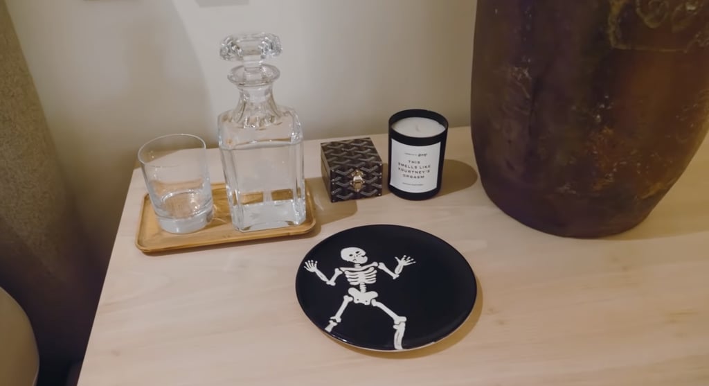 On his nightstand is a skeleton plate that Kardashian made at Color Me Mine. Beside it is a Goop candle that says, "This smells like Kourtney's orgasm."