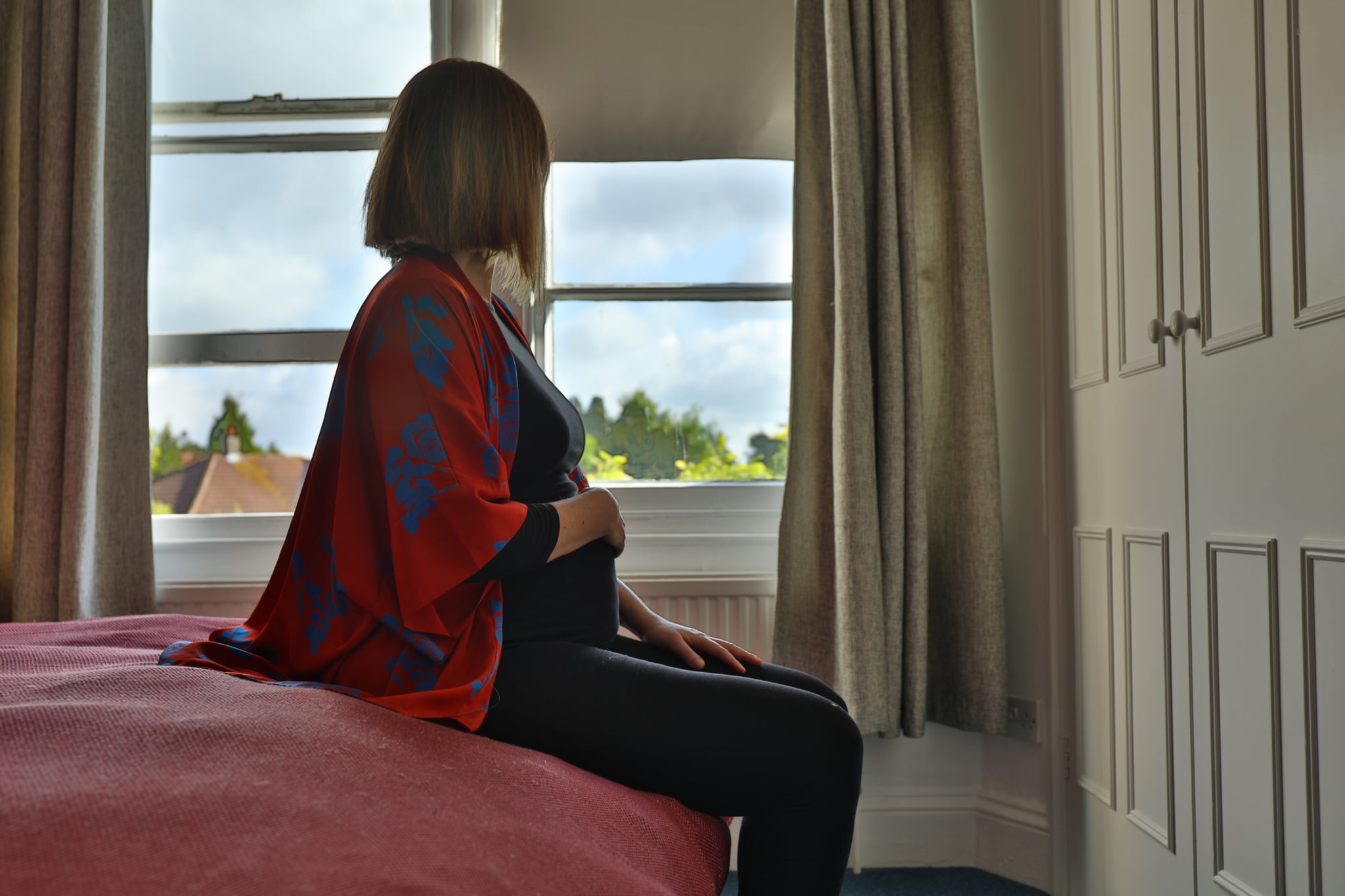 Side view of a caucasian woman pregnant in the bedroom during lockdown coronavirus with the hands on the belly