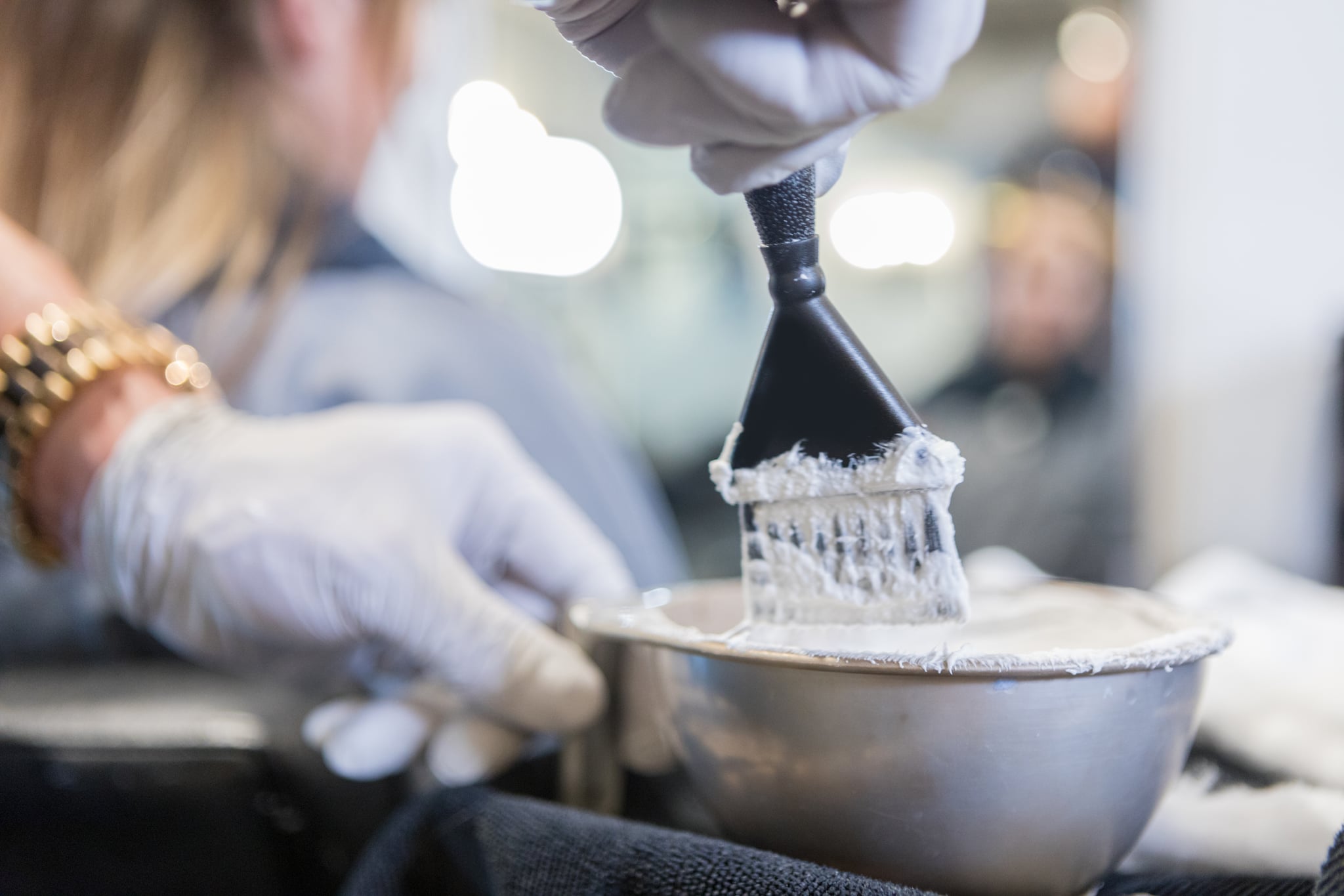 A tint brush being dipped before being used for highlighting. Female customer is in the background.