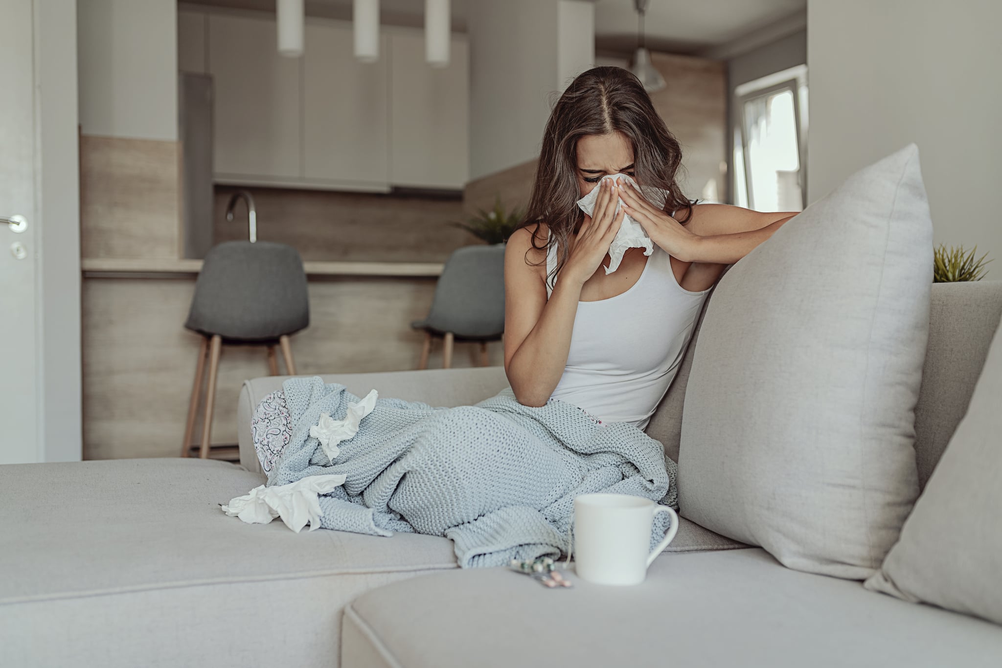 Sick Woman Covered With a Blanket Lying in Bed With High Fever and a Flu, Resting at Living Room. She Is Exhausted and Suffering From Flu. Sick Woman With Runny Nose Lying in Bed. Girl Suffering From Cold Lying in Bed With Tissue Blowing Her Nose While Sitting on the Sofa