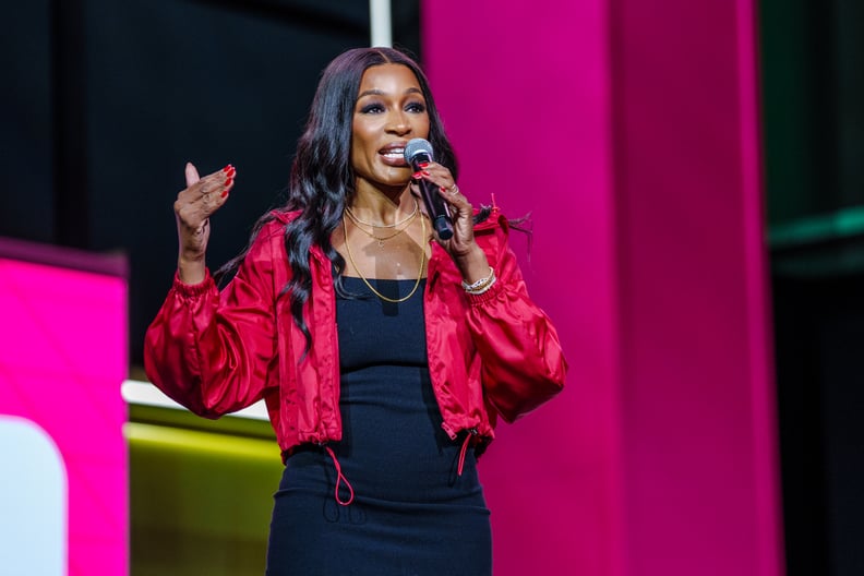 Cari Champion speaks at the Essence Festival of Culture wearing a black dress and cropped red jacket.