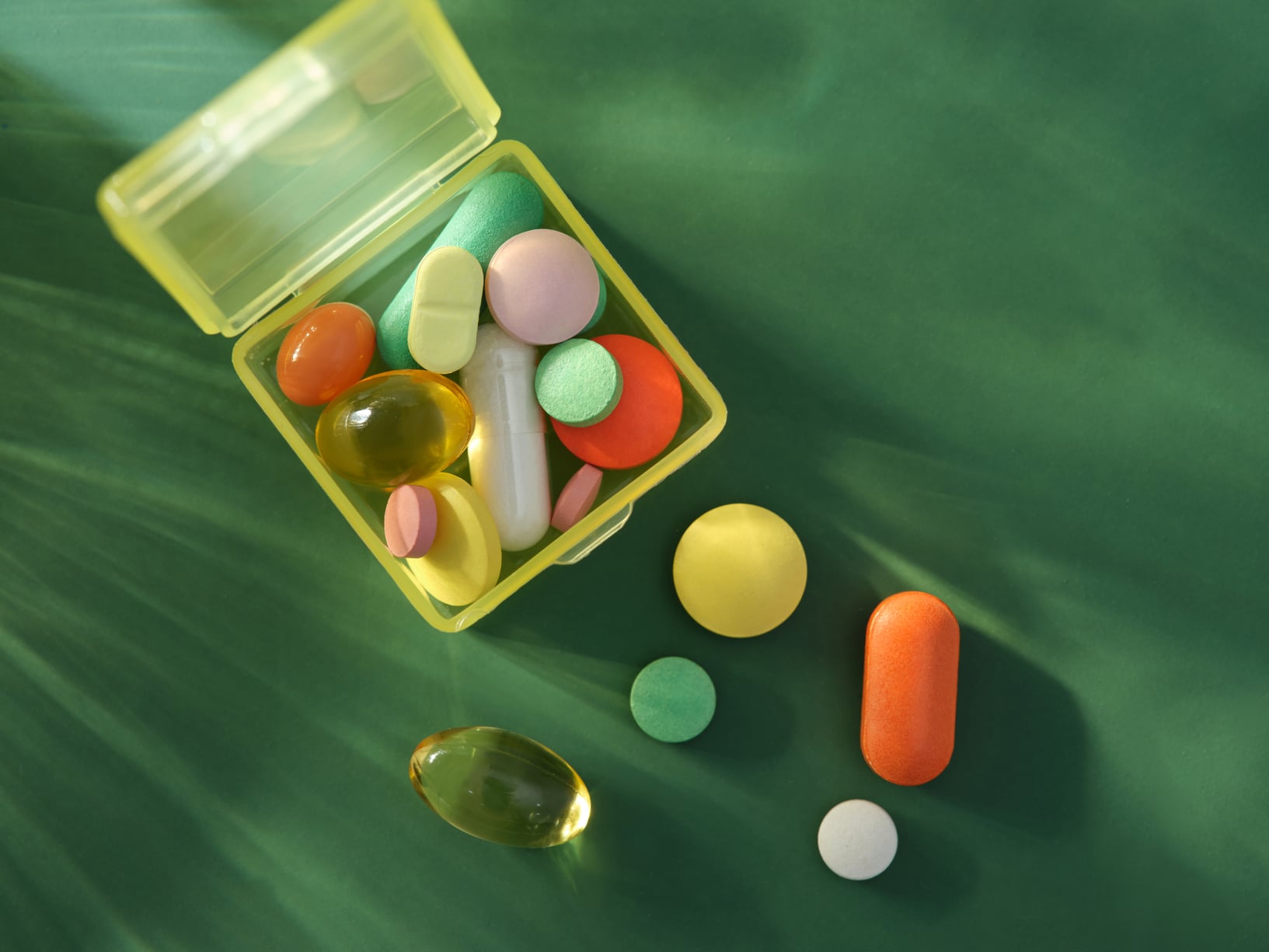 Clear box of colorful pills on a green backdrop. Clear box of colorful pills on a green backdrop.