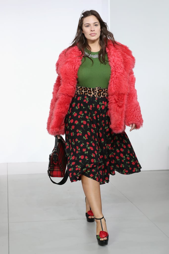 Walking in Michael Kors wearing a fuzzy jacket, green top, and floral skirt.